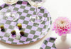 A checkered tray with two wine glasses and five olives. A pink flower is next to the tray.