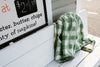 Green and white checkered jacket draped over a bench next to a menu sign displaying prices and items.