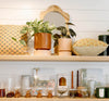 A shelf displaying plants, pillows, glassware, candles, and decorative items. A wooden mirror is centered above the items.