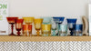 A shelf displaying a variety of colored glassware, including glasses in red, orange, yellow, green, and blue hues, arranged in a row against a light-colored wall.