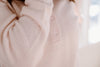 Close-up of a person wearing a light pink sweater with three buttons on the front placket.