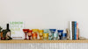 A wooden shelf displays a row of colorful glasses, a bottle of wine, a book titled 