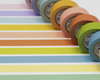 Seven rolls of colored tape arranged side by side on matching horizontal striped paper.