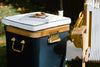 A navy and wood cooler with a white cushion top holds a book titled 