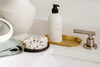 Bathroom counter with a soap dispenser on a tray, a washcloth, a mirror, and a speckled soap bar near a metal faucet.