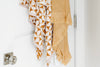 Two patterned towels hang on a white door. One towel has white and brown geometric designs, and the other is beige with fringes.