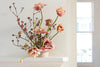 A floral arrangement with pink tulips and branches in a pale vase on a white mantel.