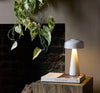 A white table lamp on a wooden surface, next to a book titled 