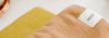 Close-up of two folded towels, one yellow with a waffle texture and another light brown with a smooth texture, featuring a 