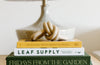 A lamp and three books stacked on a table. A decorative knot ornament sits on top of the books.