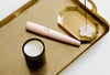 A pink electric lighter, a lit candle, and an incense holder with burning incense are arranged on a gold tray.