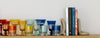 A wooden shelf with colorful glasses on the left and five books supported by stone bookends on the right.