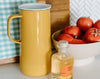 A yellow pitcher, a bottle of apple cider vinegar, and a bowl of tomatoes are placed on a kitchen counter.