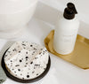 White lotion bottle on a gold tray next to a speckled black and white object on a black base.