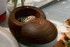 A wooden salt cellar is open on a table next to a plate of bruschetta topped with avocados and radishes.