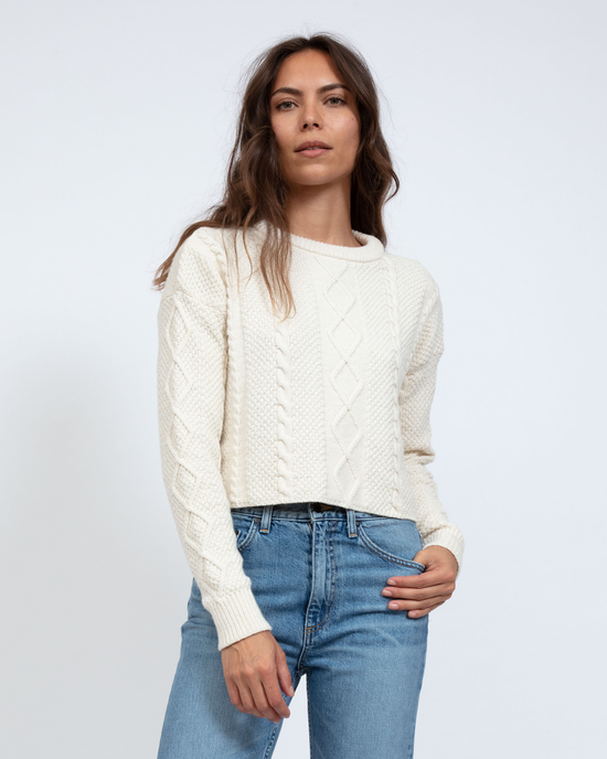 A woman in a white Cable Cropped Crew sweater from ASKK NY and blue jeans standing against a light background.