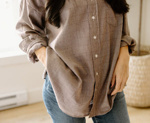 Person wearing a brown plaid button-up shirt and blue jeans with hands in pockets.