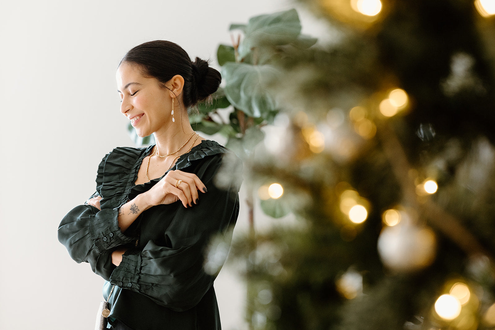 A woman in a dark blouse stands with eyes closed, smiling. A decorated, out-of-focus Christmas tree is visible in the foreground.