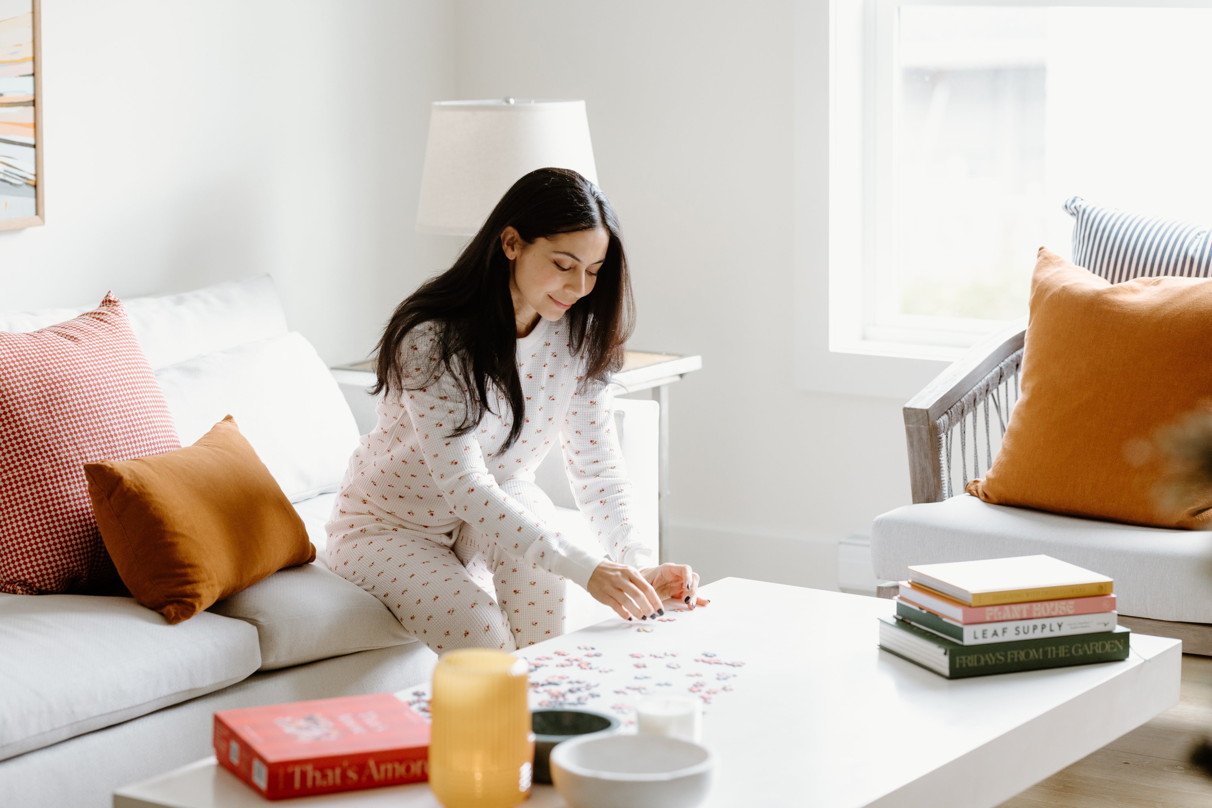 Model wearing pajamas in living room setting doing a puzzle.