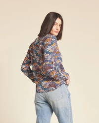 Woman modeling a floral Trovata Birds of Paradis Jacquelin Shirt in Bijou Glade and denim jeans, looking over her shoulder.