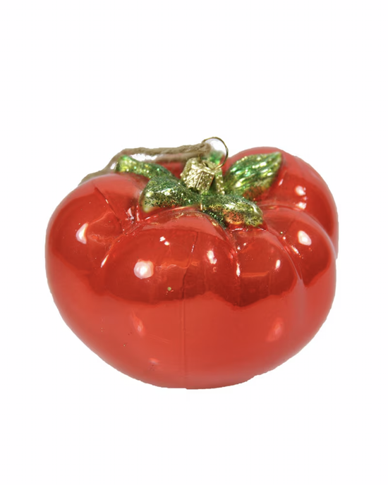 The Tomato Ornament, an exquisite glass creation by Cody Foster, features a shimmering red hue with delicate green leaves and a gold hanging loop, making it a timeless addition to their collection of handcrafted decorations.