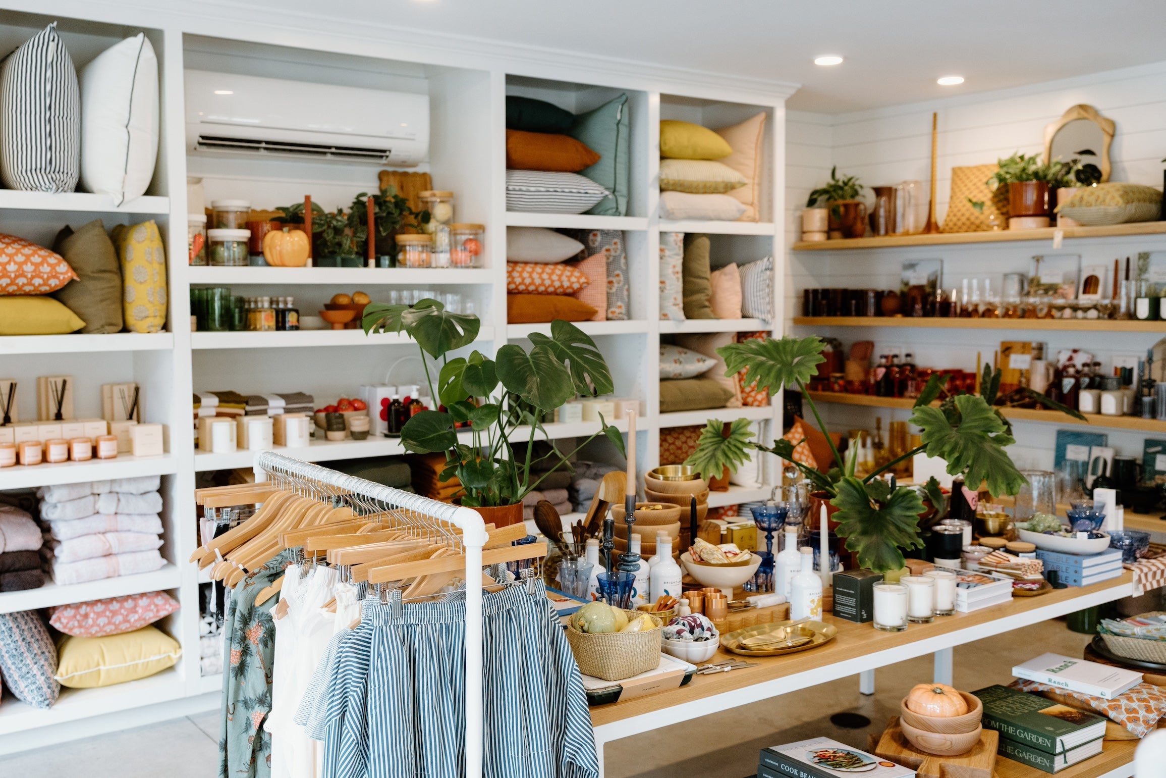 A neatly arranged store display with shelves of home goods, including pillows, plants, clothing, candles, and various decor items.