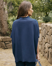 Woman in a Frank & Eileen Audrey Funnel Neck Capelet in Air Force blue top standing in a garden.