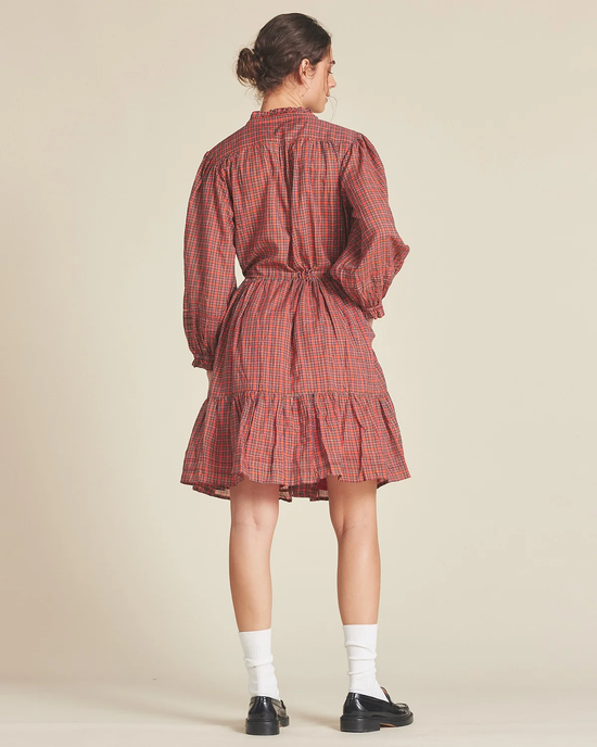 A person standing with their back to the camera, wearing a Yulia Dress in Redford Plaid by Trovata Birds of Paradis with a 2-tiered skirt and ruffled hemline, white socks, and black shoes.
