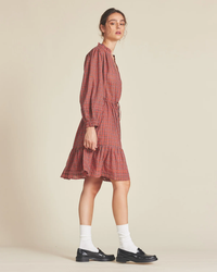 A woman wearing a Trovata Birds of Paradis Yulia Dress in Redford Plaid with a 2-tiered skirt, white socks, and black lace-up shoes standing against a neutral background.