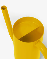 The product features the Tango Watering Can - Short Yellow by Areaware, designed from powder-coated steel, showcasing a vibrant yellow hue with a long spout and semicircular top opening, set against a plain background.