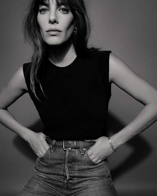 A black and white image of a person with long hair wearing the Patti Muscle Tank in Jet Black by Nation LTD and high-waisted jeans, standing with hands on hips.