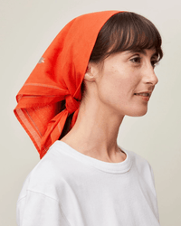 A person wearing a white shirt and the Moismont Bandana No 656 in Poppy Red gazes to the side against a plain background.