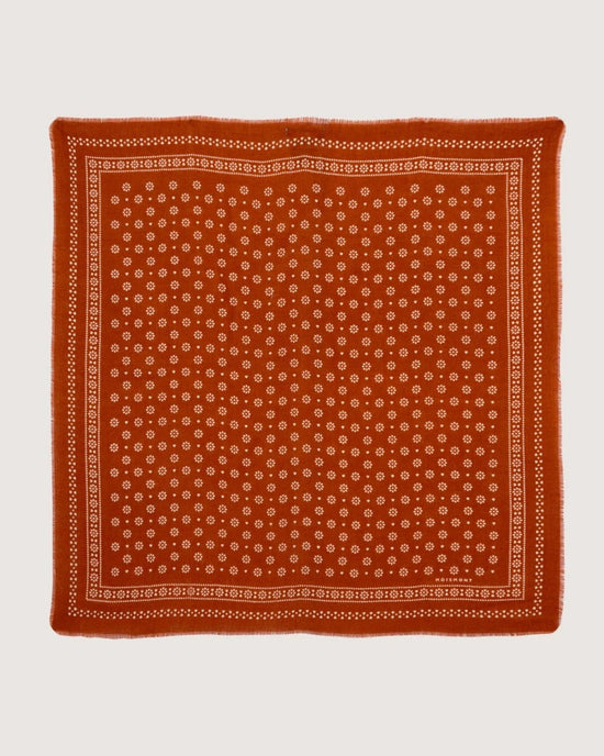 The Bandana No 676 in Brick by Moismont is a square red bandana, crafted from 100% wool, featuring a white floral and dotted pattern with a detailed border.