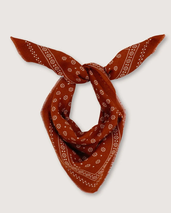 The Bandana No 676 in Brick by Moismont, made from 100% wool, showcases intricate white patterns and floral designs. This exquisite scarf is elegantly tied in a loose knot and displayed on a plain background.