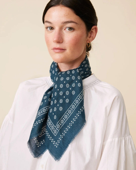 A woman wearing a white blouse and a luxurious Moismont Bandana No 676 in navy blue, featuring intricate screen-printed patterns, poses elegantly against a neutral background.