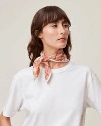 A person wearing a handcrafted white t-shirt and the Moismont Bandana No 712 in Pop Pink, looking to the side against a plain background.