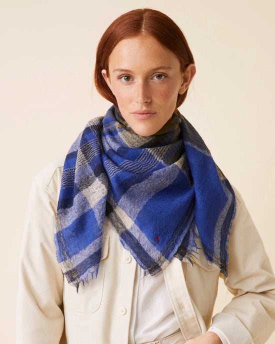 A person stands against a neutral background, gracefully adorned with the oversized Bandana No 752 in Royal Blue from Moismont, styled over a light-colored jacket.