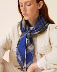 A person with long red hair, wearing a cream-colored shirt and an oversized Moismont Bandana No 752 in Royal Blue, which exudes handwoven beauty, looks down.