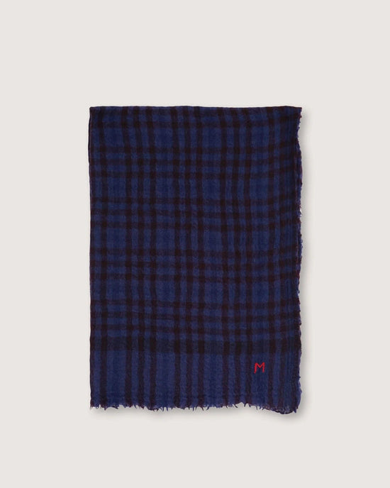 The Scarf No 754 in Navy Blue by Moismont is a hand-woven wool accessory with a blue and black plaid pattern, frayed edges, and a small red "M" embroidered near one corner, capturing the essence of Moismont’s iconic designs.