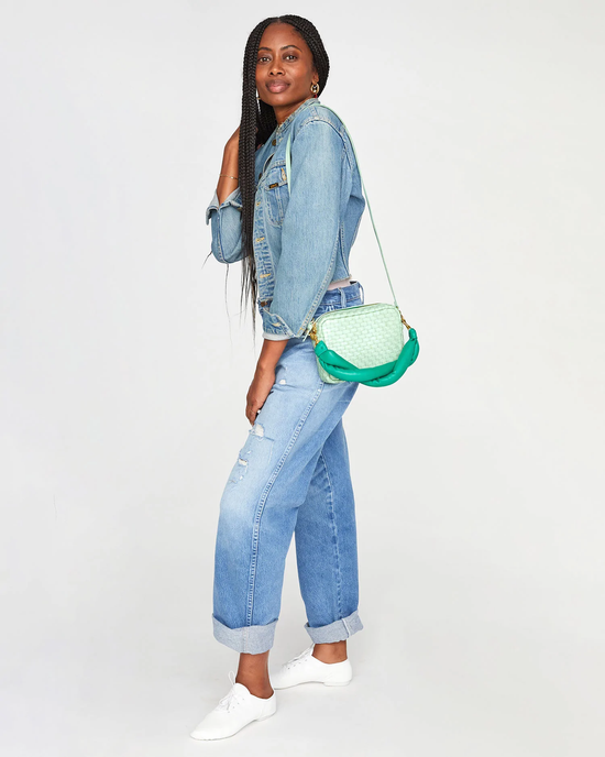 Woman in denim outfit posing with a green Clare V Midi Sac in Mist Woven Checker featuring a crossbody strap.