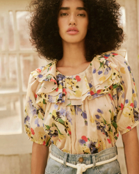 Woman in The Sunrise Top in Bright Grove Floral by the Great and denim jeans standing against a neutral backdrop.