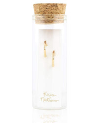 The Classic Huggie Hoops in Gold by Kris Nations are elegant, minimalist hoop earrings presented in a transparent glass container with a cork lid and labeled with the brand name.