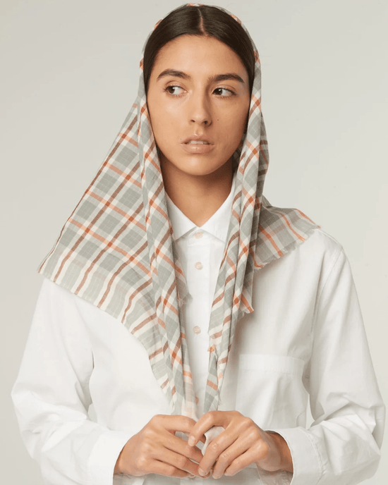 A person in a white shirt wears an oversized Plaid Bandana in Cloud by Moismont draped over their head, looking to the side against a plain background.