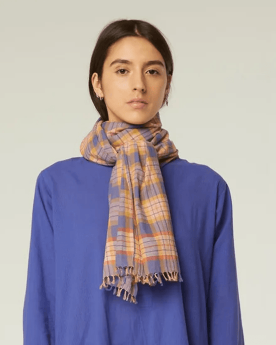 A person is wearing a blue top and a Varied Plaid Scarf in Pansy Blue by Moismont, set against a neutral background.